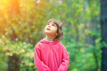 Portrait of a little girl outdoor in the forest in autumn. Girl looking up