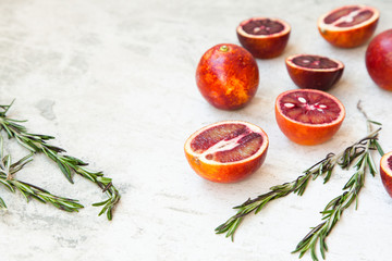 Red Sicilian orange whole and cut on a light background with branches of rosemary. Daylight, open space for your text.