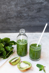 Green cocktail in a bottle and in a glass with spinach, mint, rosemary, kiwi and apple on a light background.