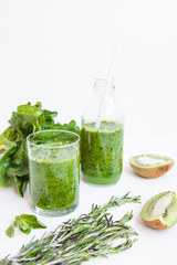 Green cocktail in a bottle and in a glass with spinach, mint, rosemary, kiwi and apple on a light background.