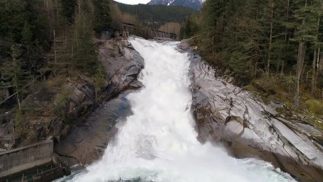 Raging Waterfall Aerial with Snowy Mountain in Background and Mist from White Water Snow Melt