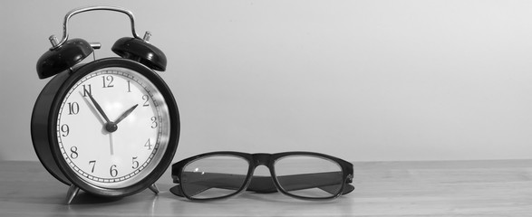 Alarm clock and glasses on wooden table.
