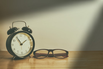 Alarm clock and glasses on wooden table. - Powered by Adobe