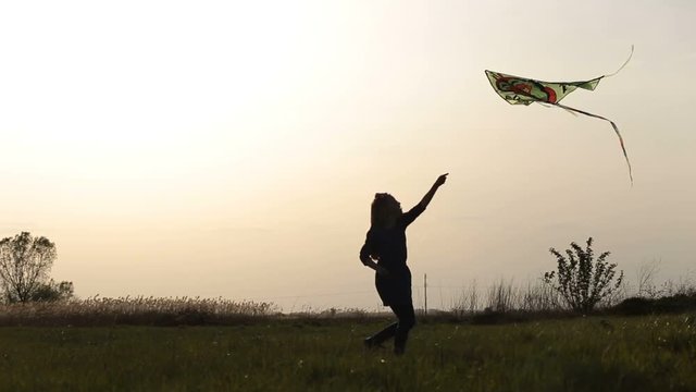 Cute little girl flying a kite in meadow at sunset