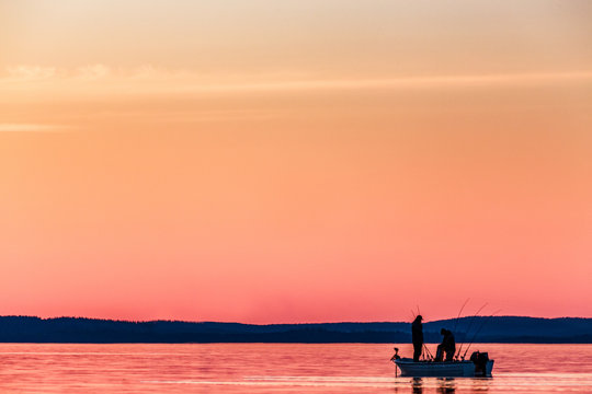 Two People Fishing From Small Boat At Sunset