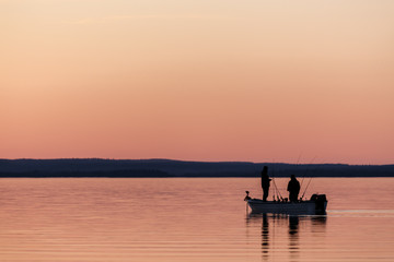 Naklejka na ściany i meble Two people fishing from small boat at sunset