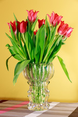 Scarlet tulips in a crystal vase on a yellow background