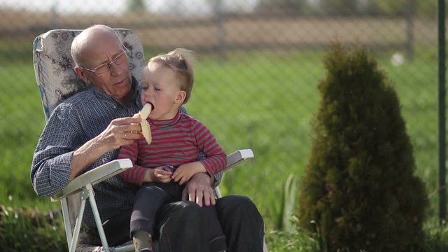 Grandfather giving banana to his grandson outdoor.