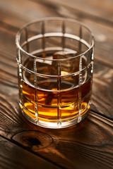 Glass of whiskey with ice cubes on wooden table