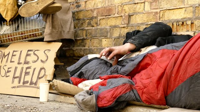 Homeless man turns around during sleep, cart with his stuff is near him.