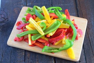 Freshly cut red, yellow, green paprika on a wooden cutting board with a wooden background. Step by step cooking