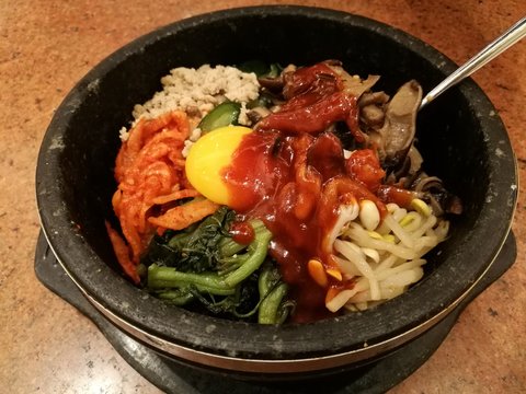 Classic Korea food vegetable Bibimbap hot stone pot,rice carrot,spinach,mushroom,cucumber,seaweed,raw yolk egg ,hot spicy chili sauce with spoon,focus-on-foreground blur background,Asian meal