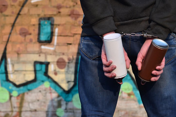 A rear view of an arrested street artist in handcuffs with aerosol paint can