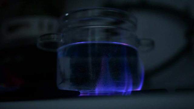 Water boiling in glass pot at gas stove, blue flame illuminate bottom of the pot