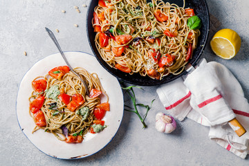 Whole-grain tomato pasta with basil pesto on cast iron pan with one white ceramic plate, lemon and...
