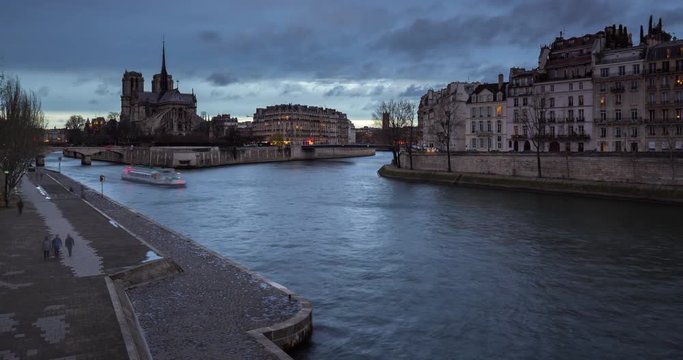 The Seine River banks by Ile Saint Louis and Ile de la Cite with Notre Dame Cathedral (time-lapse). City lights illuminating at twilight. Paris, 4th Arrondissement, France