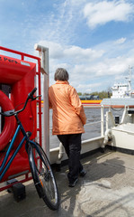 Seniorin fährt mit der Kanalfähre über den Nord-Ostsee-Kanal in Schleswig-Holstein, Fahrradtour auf dem Radfernweg