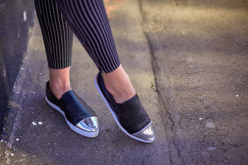 Female legs, the girl walks along the asphalt in black shoes and narrow black jeans in white stripes