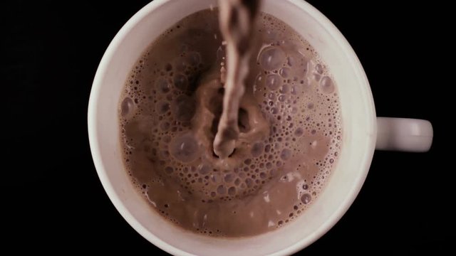 Slow mo. In a cup abundantly pour a lot of cocoa, a top view, on a black table
