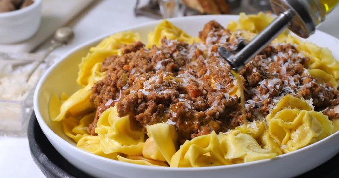 Pouring olive oil over delicious steamy tortellini in bolognese sauce