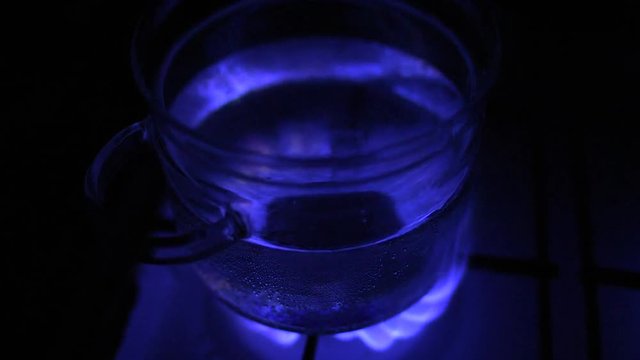 Water boiling in glass pot at gas stove, blue flame illuminate bottom of the pot