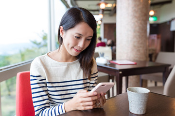 Woman sending sms on cellphone in cafe