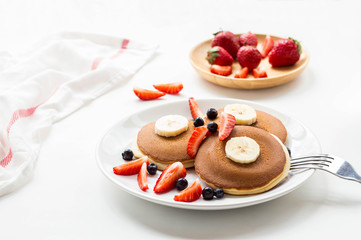 Summer dessert of pancakes with fresh fruit, banana, blueberries, strawberry on white background
