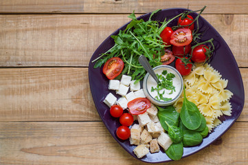 Pasta salad with farfalle, red cherry tomatoes, arugula, feta cheese, chicken meat and baby spinach served on a big plate with white sauce Balanced and healthy meal