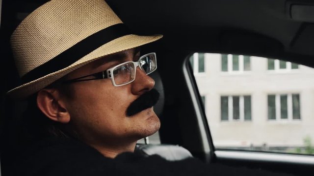 Adult man with mustache in hat, glasses sitting in car. Summer day. Parody. Close up