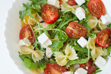 Pasta salad with farfalle, cherry tomatoes, rocket leaves, spinach, chicken meat and feta cheese in white bowl. Healthy salad. Balanced meal