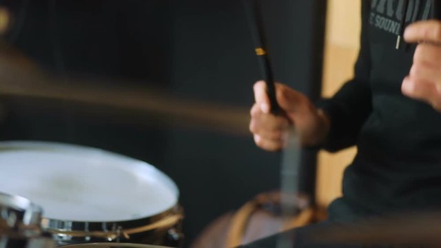Studio man from band in black modern sweatshot playing on the drums and drum-type plates