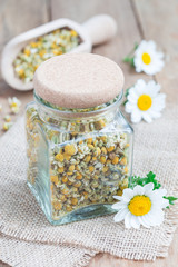 Dry herbal chamomile tea in a jar with fresh chamomile flowers on background, vertical