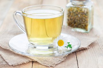 Chamomile tea in glass cup, chamomile flowers and dry tea on background, horizontal