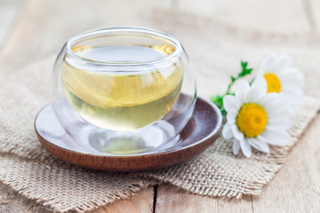 Obraz na płótnie Canvas Chamomile tea in glass cup, chamomile flowers on background, horizontal
