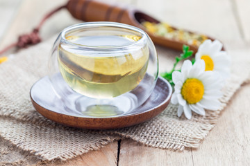 Chamomile tea in glass cup, chamomile flowers and dry tea on background, horizontal