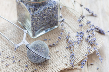 Dry lavender tea in tea infuser spoon and glass jag on wooden background, horizontal