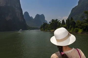 Gordijnen Woman with a hat looking at the landscape in a river cruise in the Li River between Guilin and Yangshuo, in China  Concept for travel in China © Tiago Fernandez