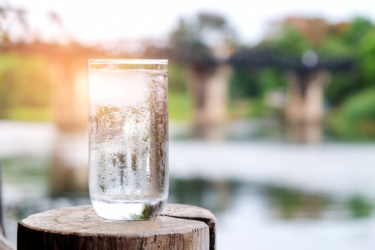 Glass of water put on wood with blurred steel bridge over the river.