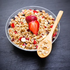 Muesli with strawberries and blueberries on dark background. Diet breakfast.