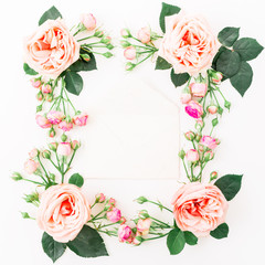 Frame made of purple roses, leaves, buds and envelope on white background. Flat lay, top view. Floral pattern of pink flowers