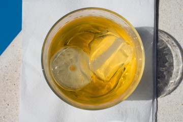 A glass of whiskey with ice near the pool with water