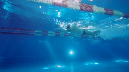 Underwater view to the professional swimmer swiming crawl stroke in the pool, reaching the wall and doing a flip turn and swims to the other side.