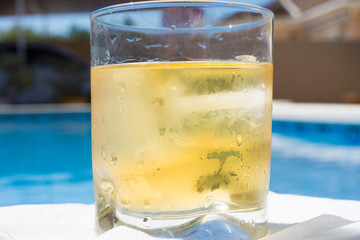 A glass of whiskey with ice near the pool with water