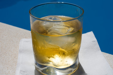 A glass of whiskey with ice near the pool with water
