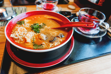 Asian cuisine - Tom kha kai or Thai coconut soup with chicken meat, rice, mushrooms, ginger and lemongrass in red bowl. Close up.