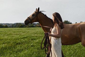 Obraz premium Authentic portrait of two friends in fresh Russian field. Young beautiful Caucasian lady in summer dress is slowly walking with gorgeous horse. Human and nature concept.
