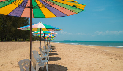 white lounge chairs with colorful sun umbrella on  beach with blue sky
