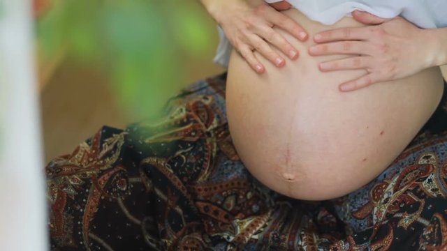 Upper-Frontal view on tender young pregnant woman swinging on gymnastic ball in room