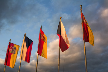 National flag of Czech Republic and Flag with coat of arms of City of Prague. Sky with dark stormy clouds in the background. Yellow evening light