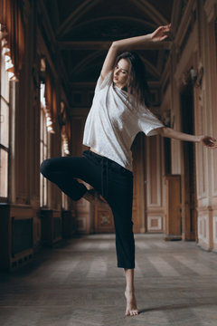 Dynamic photo of brunette sexy ballerina girl dancing in long theatre corridor. Full height of barefoot skinny dancer standing on toes in classic museum interior. Contemporary dance